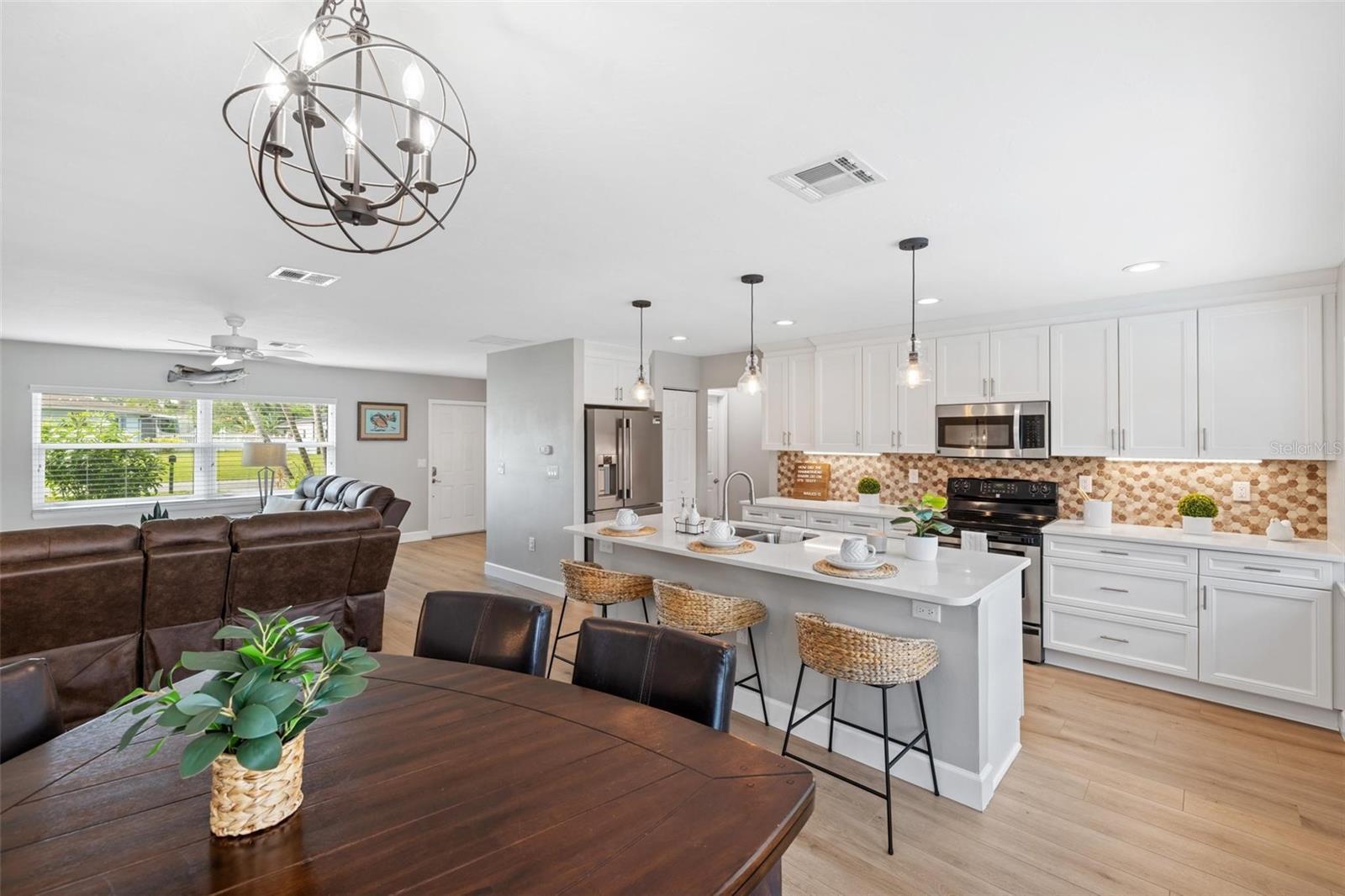 Open-plan kitchen and living room with white cabinets, a large island, and a dark wood dining table.