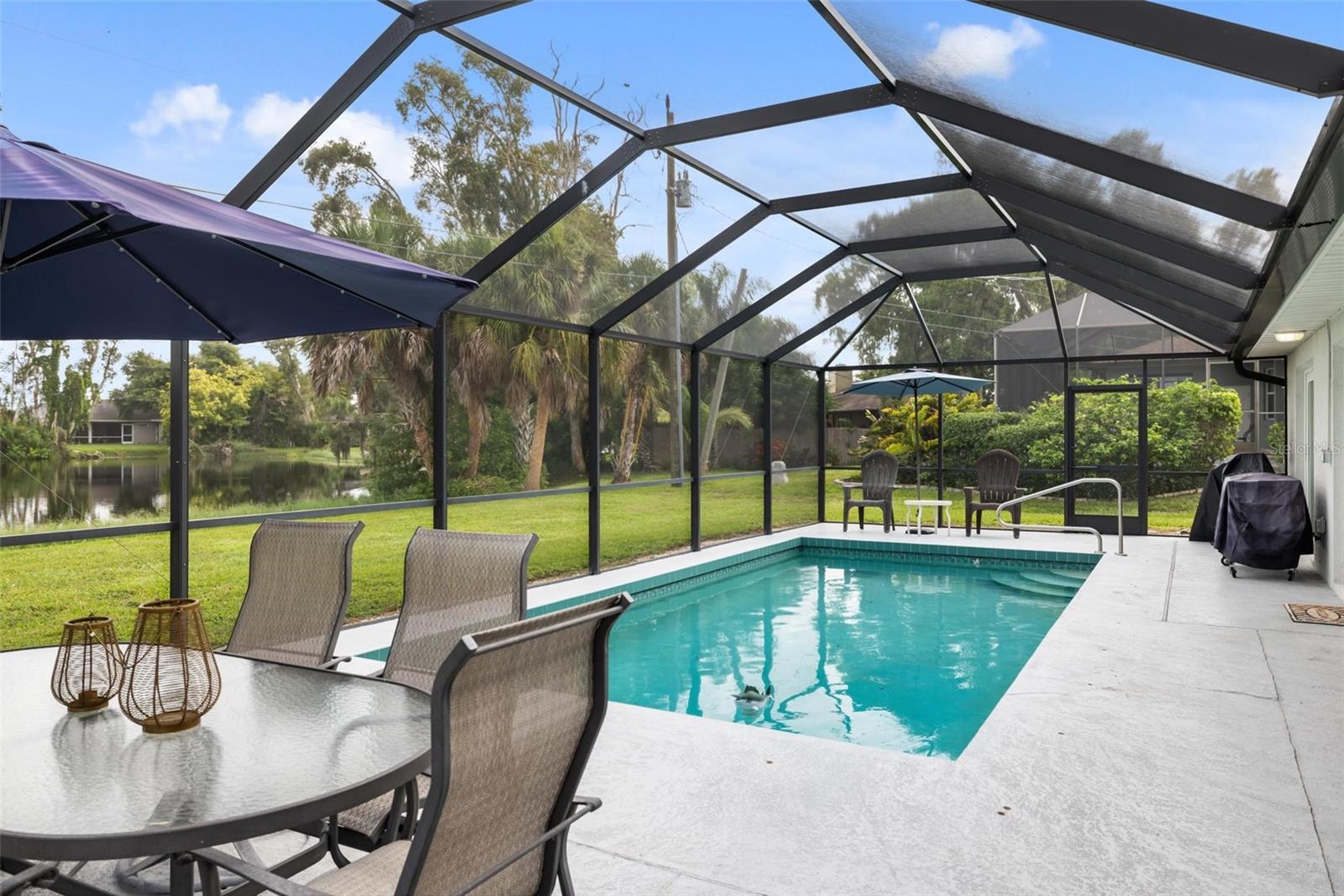 Screened backyard pool with patio furniture and a lawn bordering a pond.