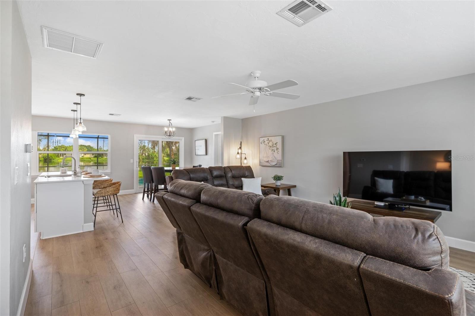 Open-plan living room with a brown sectional, kitchen island, and windows overlooking water.