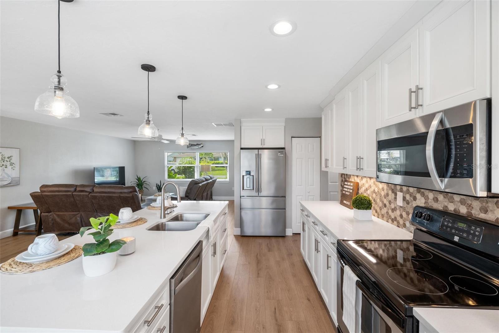 Open-plan kitchen with a white island, stainless steel appliances, and a living area with brown reclining sofas.