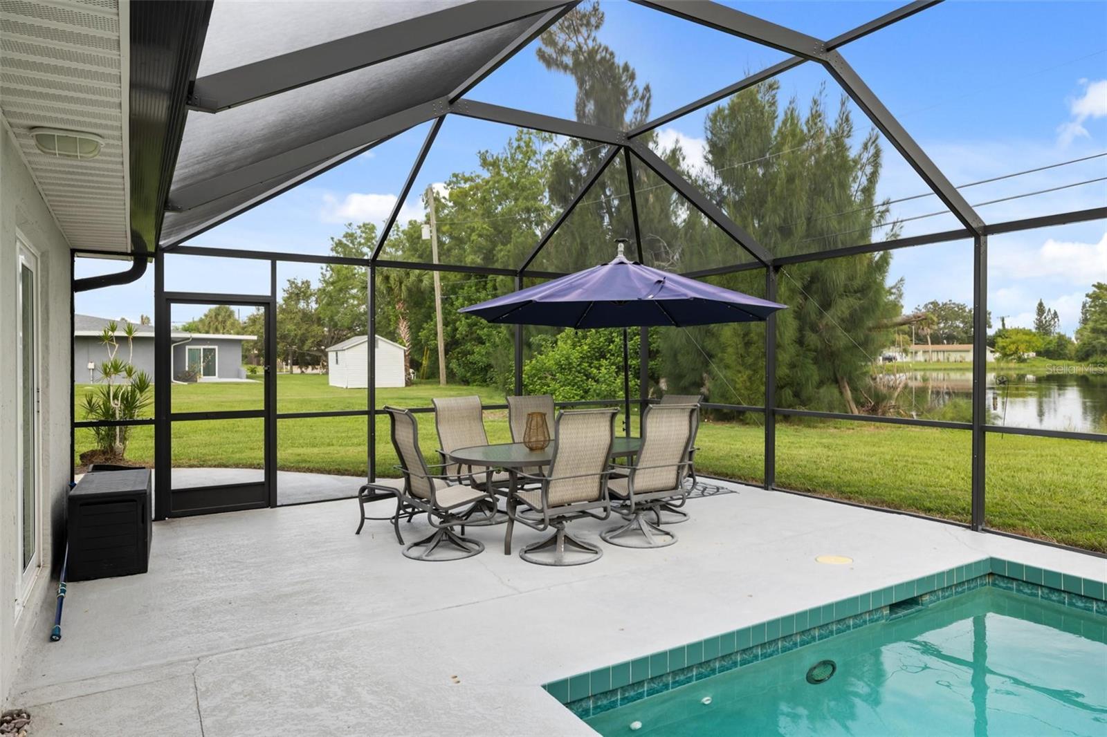 Screened pool patio with outdoor dining set and a canal beyond the grassy yard.