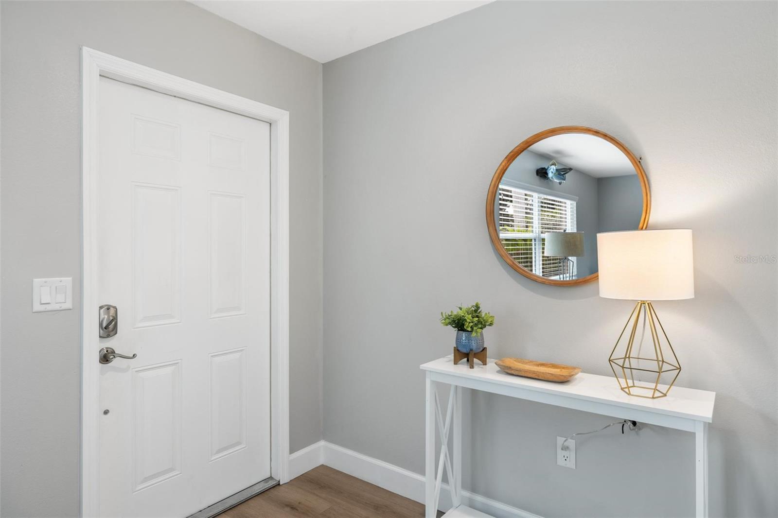 Staged entryway with a white paneled front door, console table, round mirror, and brass lamp.