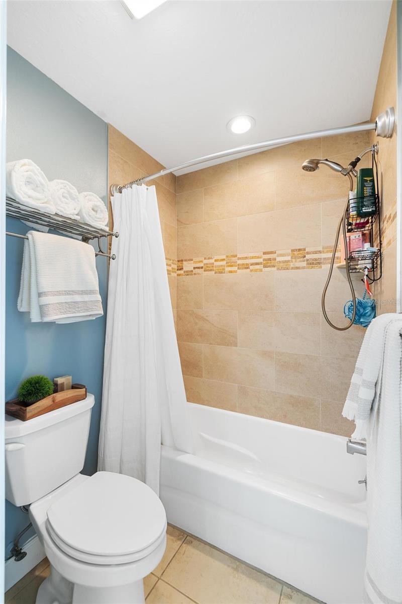 Bathroom with a tiled tub and shower, white curtain, and blue accent wall.