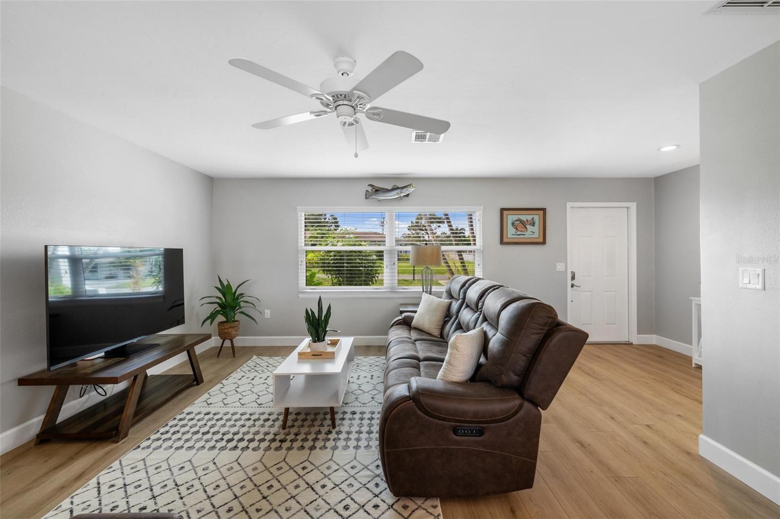 Living room with a brown leather reclining sectional, patterned rug, and window overlooking a green yard.