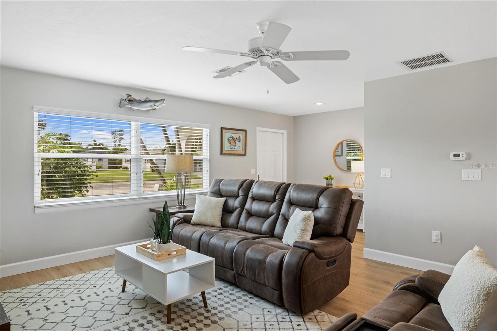 Living room with a brown leather reclining sofa, patterned rug, and wide window overlooking a green yard.