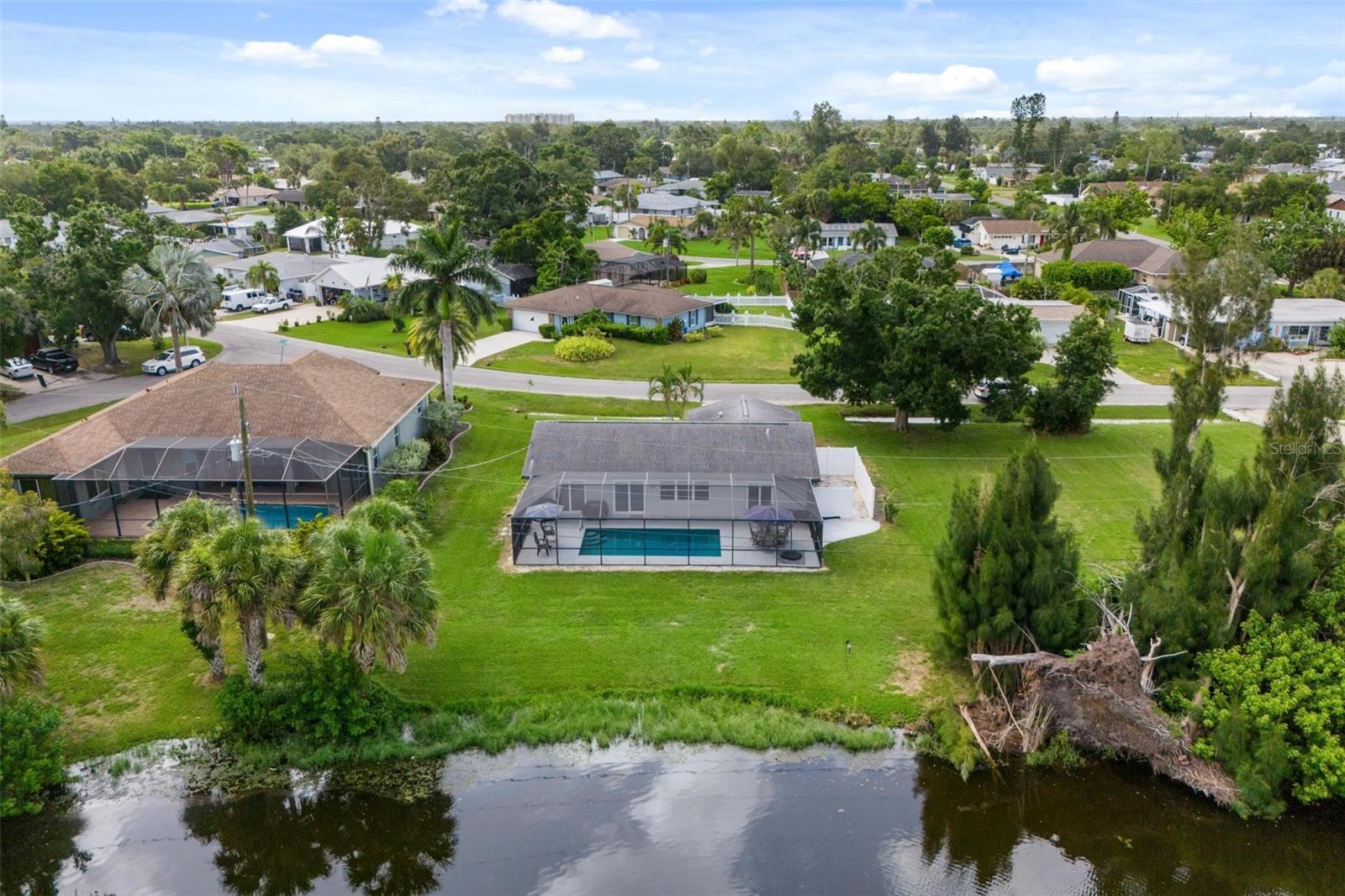 Aerial view of a home with a screened pool, broad lawn, and canal frontage.