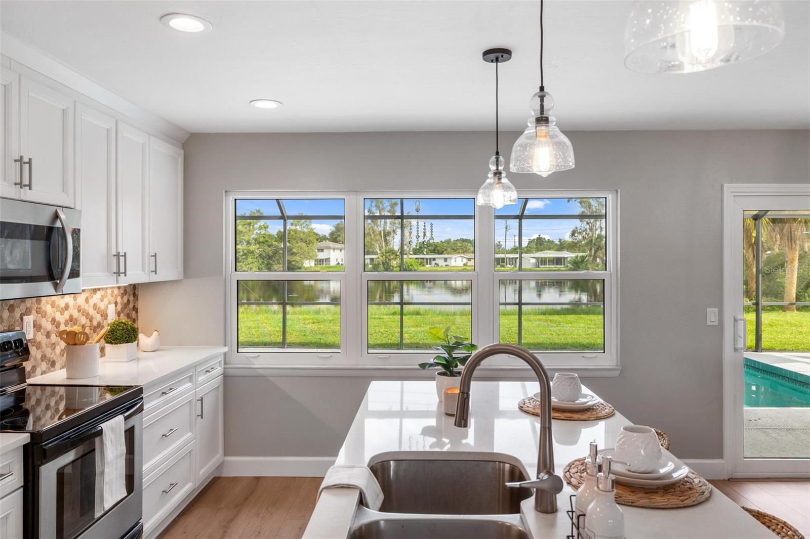 Kitchen with white cabinetry and a large window overlooking a pond; pool visible through the side door.