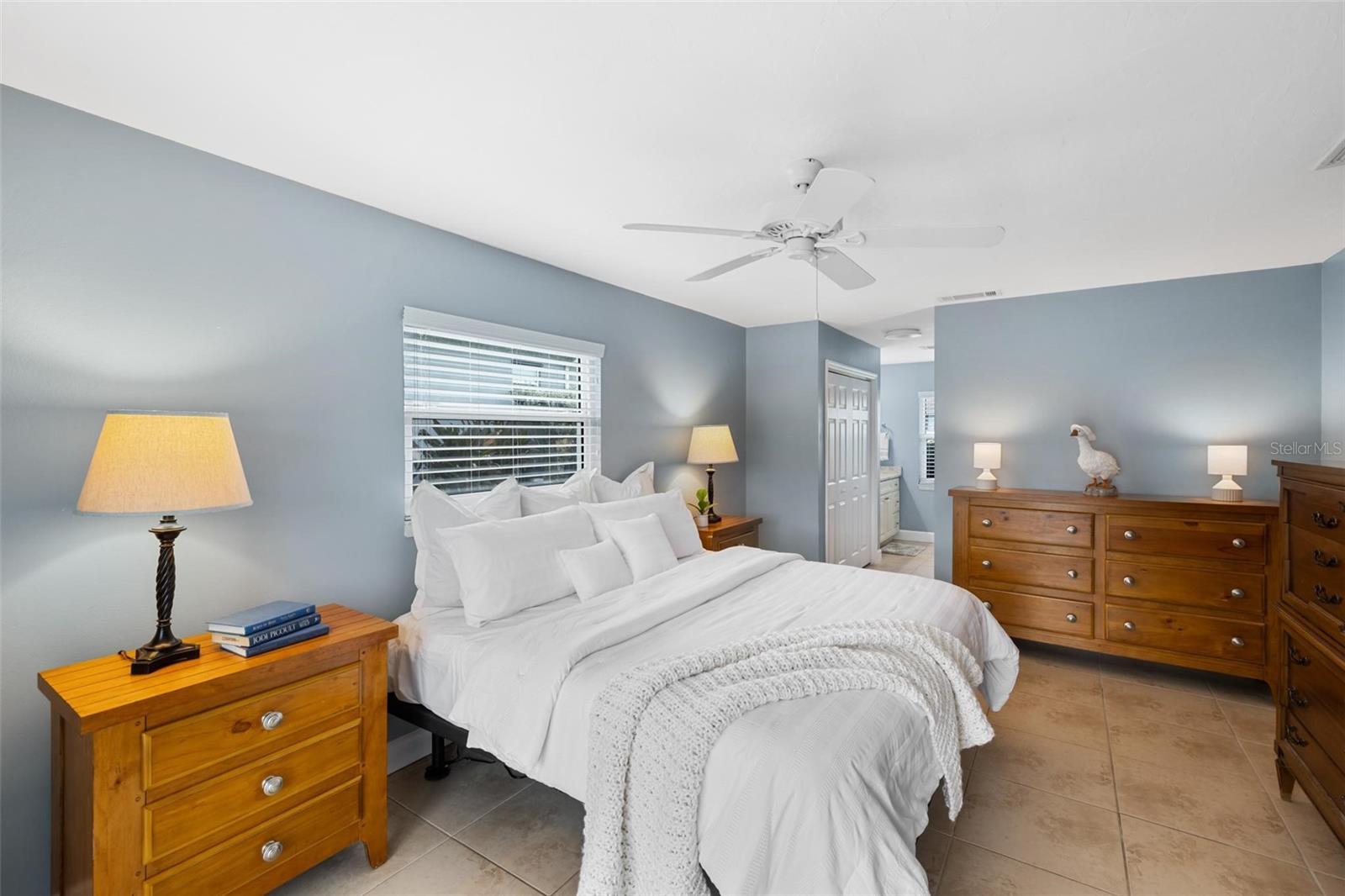 Furnished bedroom with a white bed, blue-gray walls, and matching wood dressers.