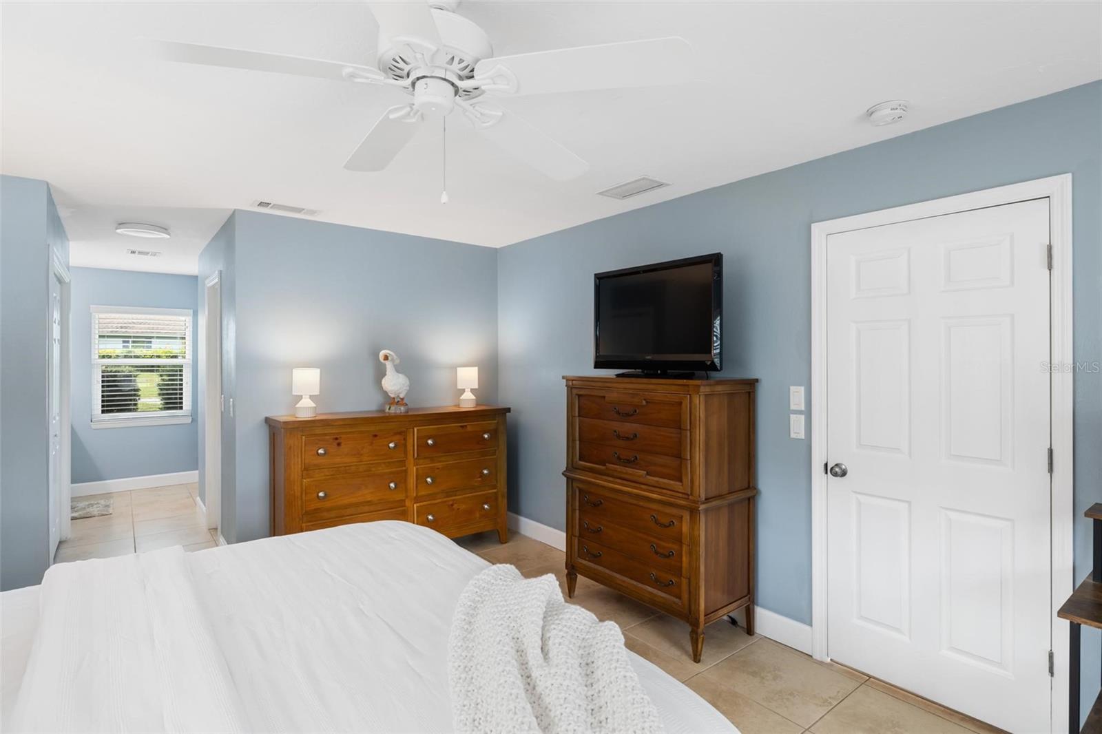 Bedroom with blue walls, wooden dressers, and a television beside the white bed.