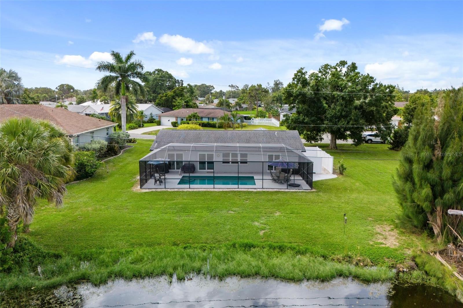 Aerial view of a home’s screened pool and expansive lawn beside a canal.