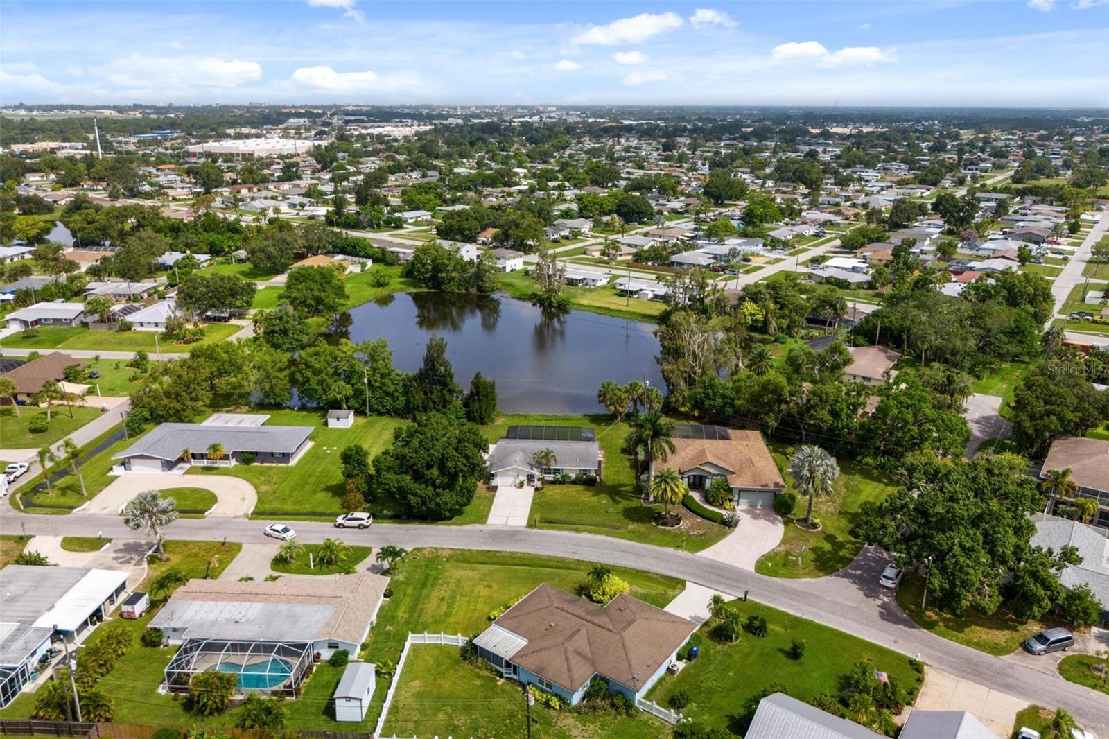 Aerial view of a residential neighborhood surrounding a pond, with homes, roads, and pools.