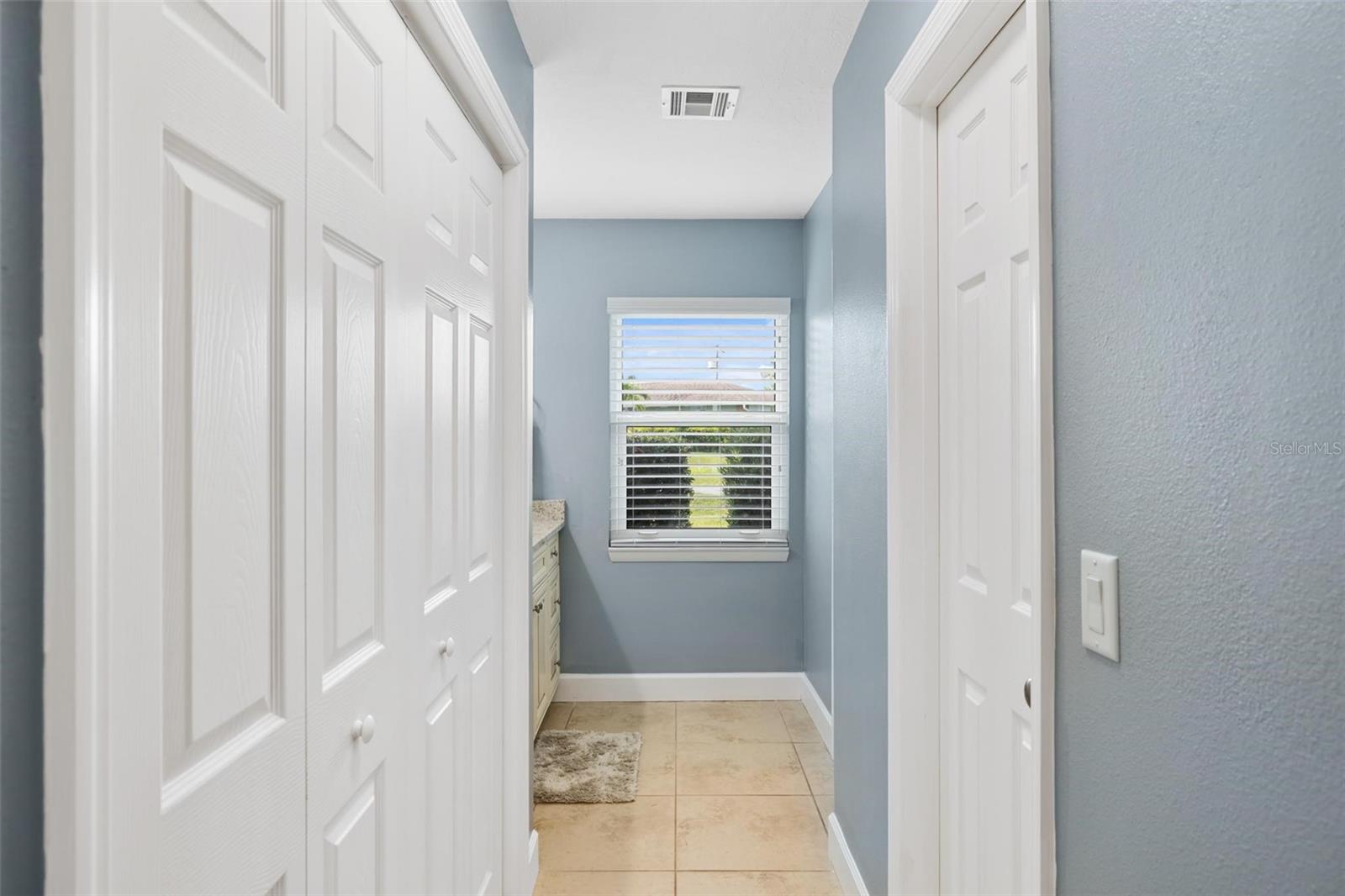 Hallway with blue walls, beige tile, white paneled doors, and a window with blinds.