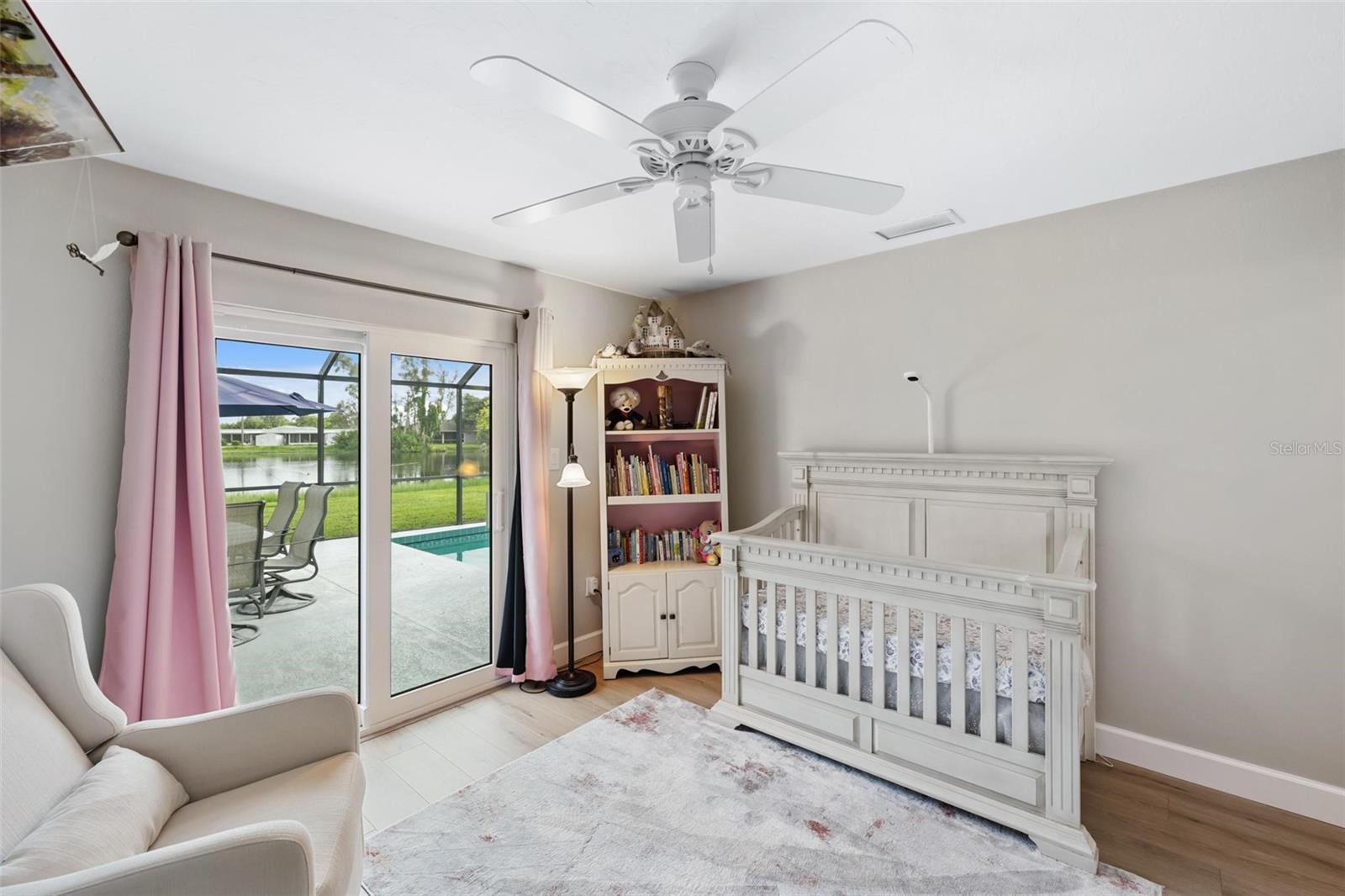 Nursery with a white crib and pink curtains opening onto a poolside patio.
