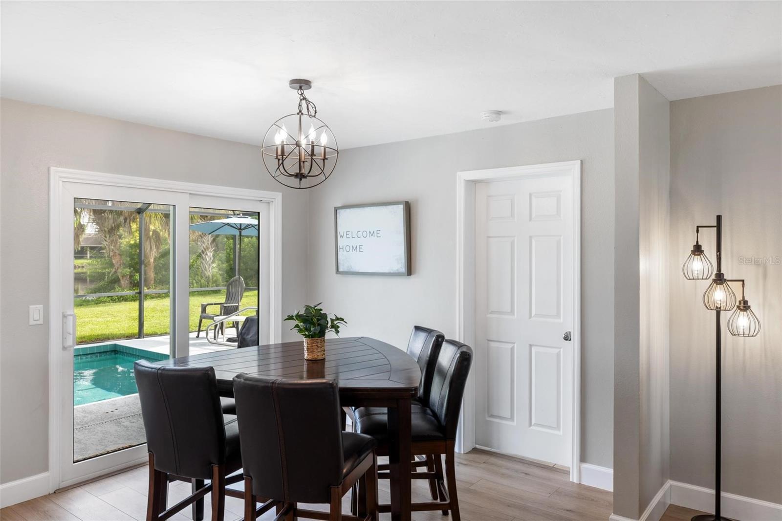 Dining room with a dark oval table and leather chairs beside sliding doors overlooking a pool.