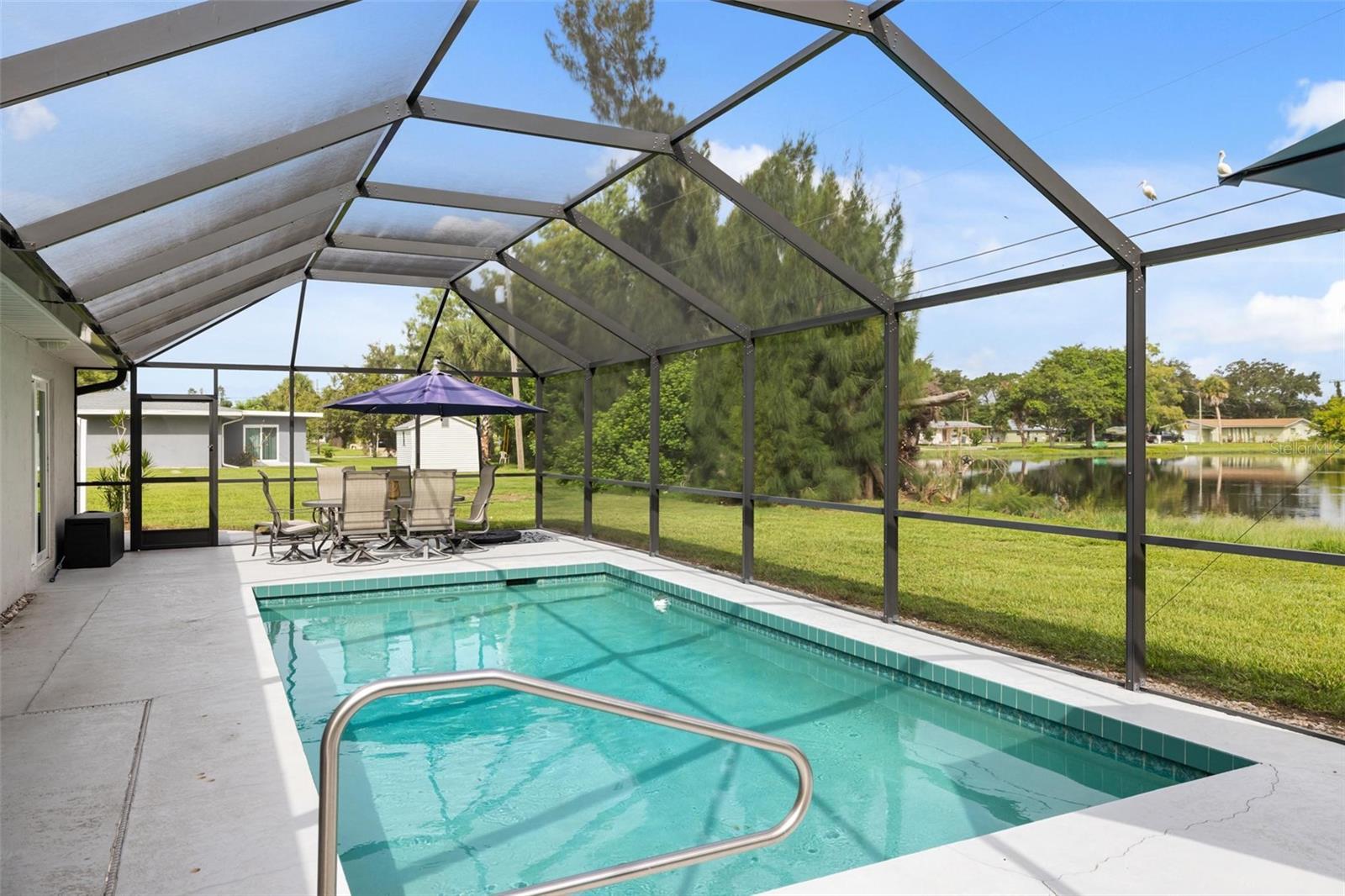 Screened-in pool and lanai with outdoor dining area overlooking a pond.
