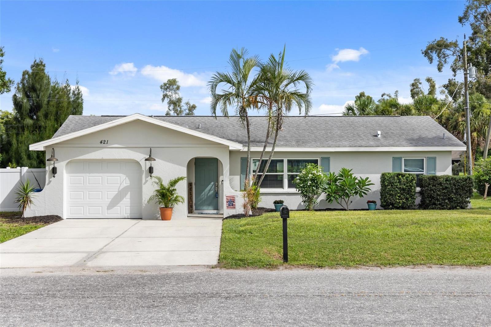Single-story home with an attached garage, palm trees, and a broad front lawn.