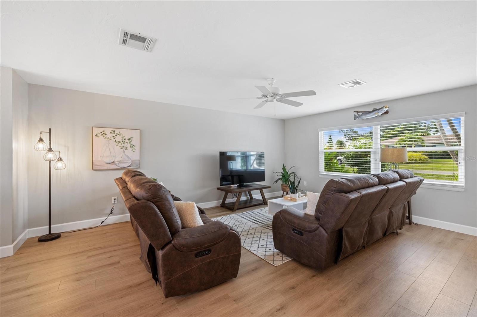 Living room with brown leather recliners, a wide garden-facing window, and light wood-look flooring.