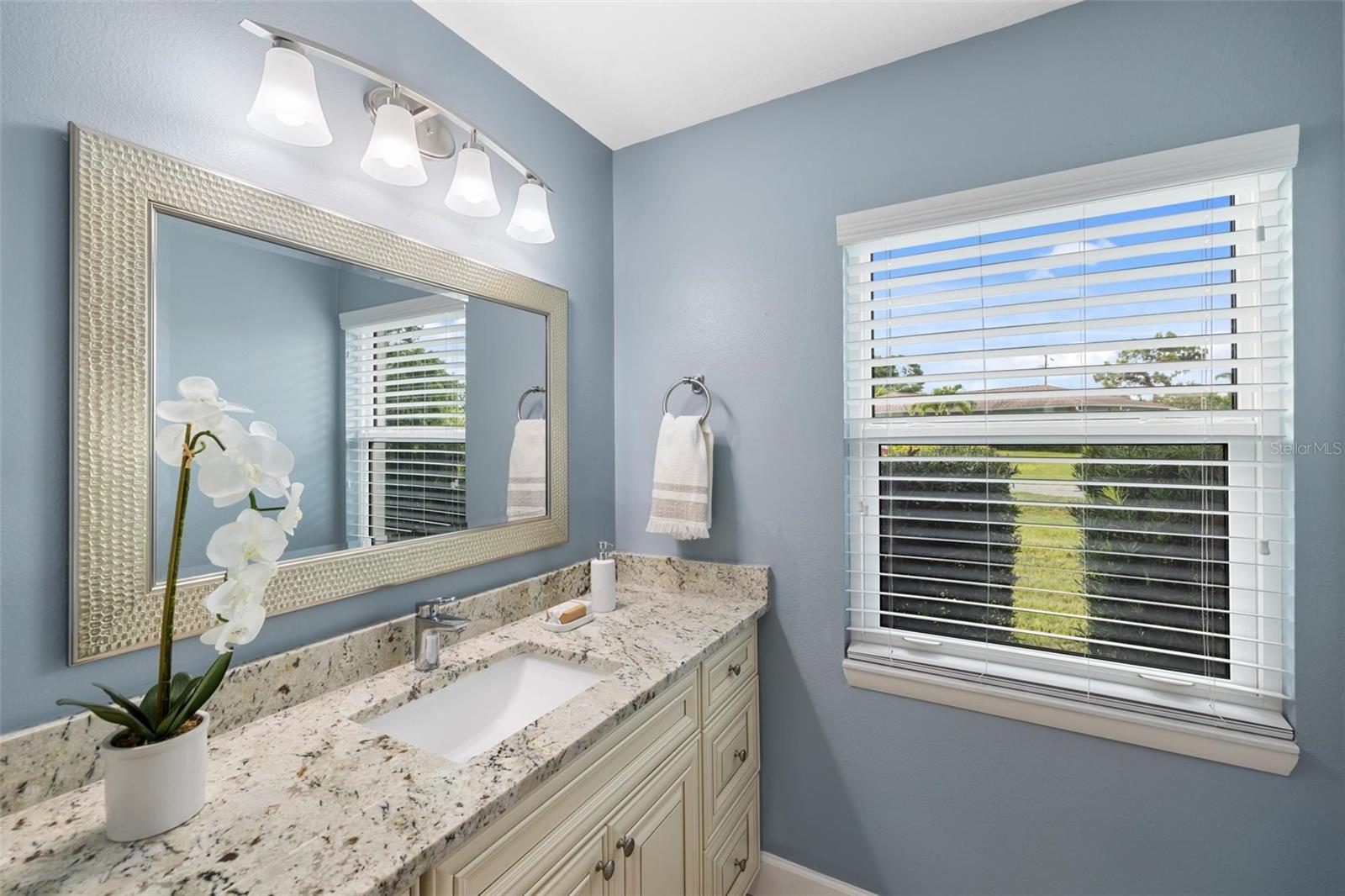 Bathroom vanity with a speckled stone counter, large mirror, and window overlooking greenery.