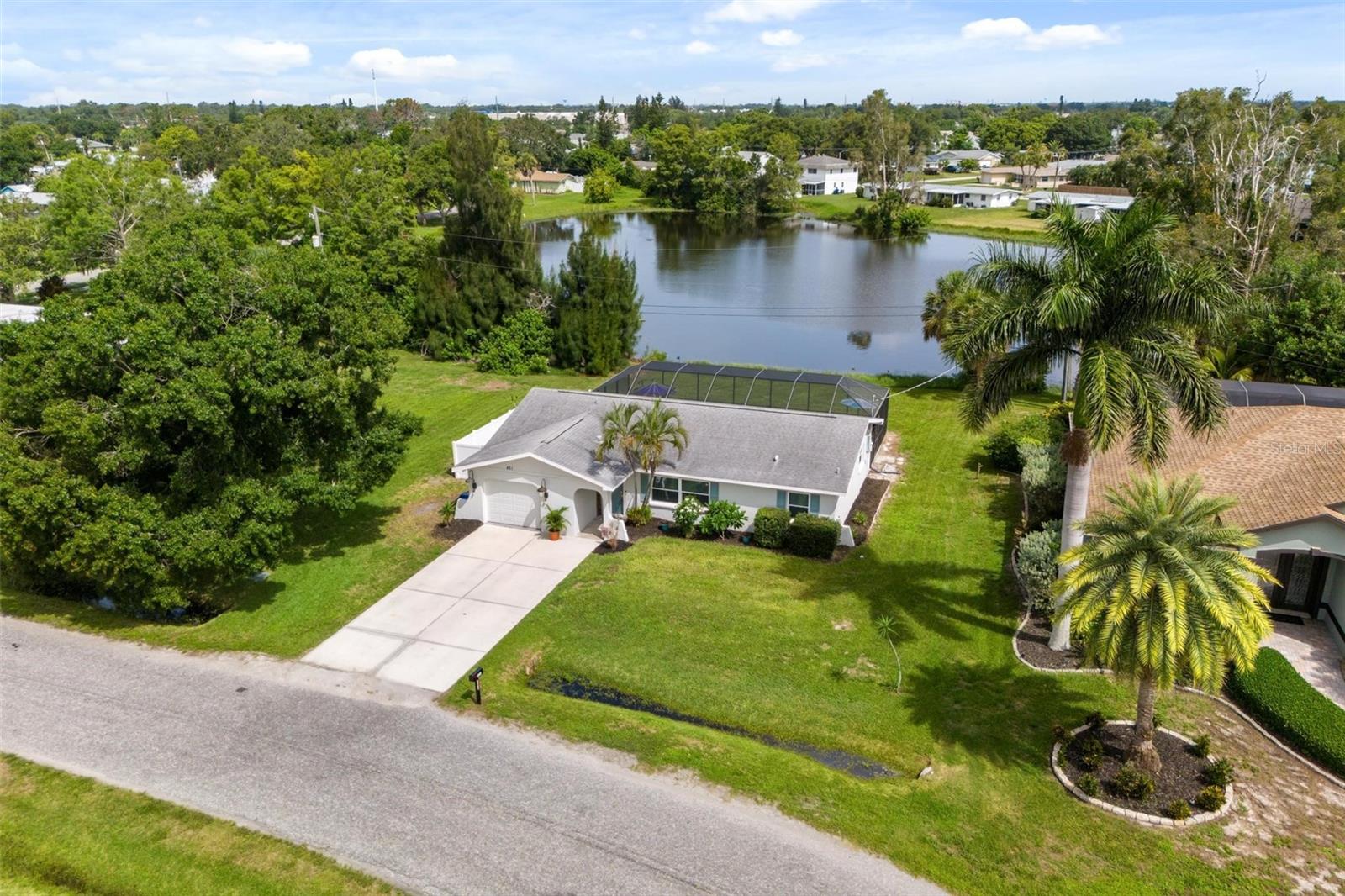 Aerial view of a white single-story home beside a pond, with a screened pool enclosure and broad lawn.