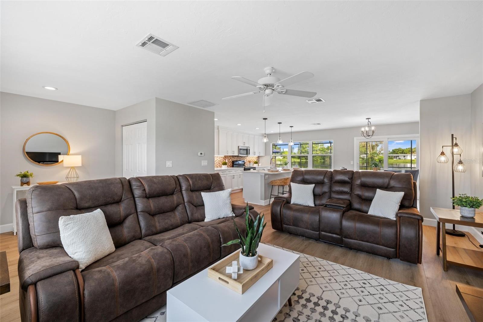 Open-plan living room with brown leather sofas, adjoining white kitchen, and water views through the windows.