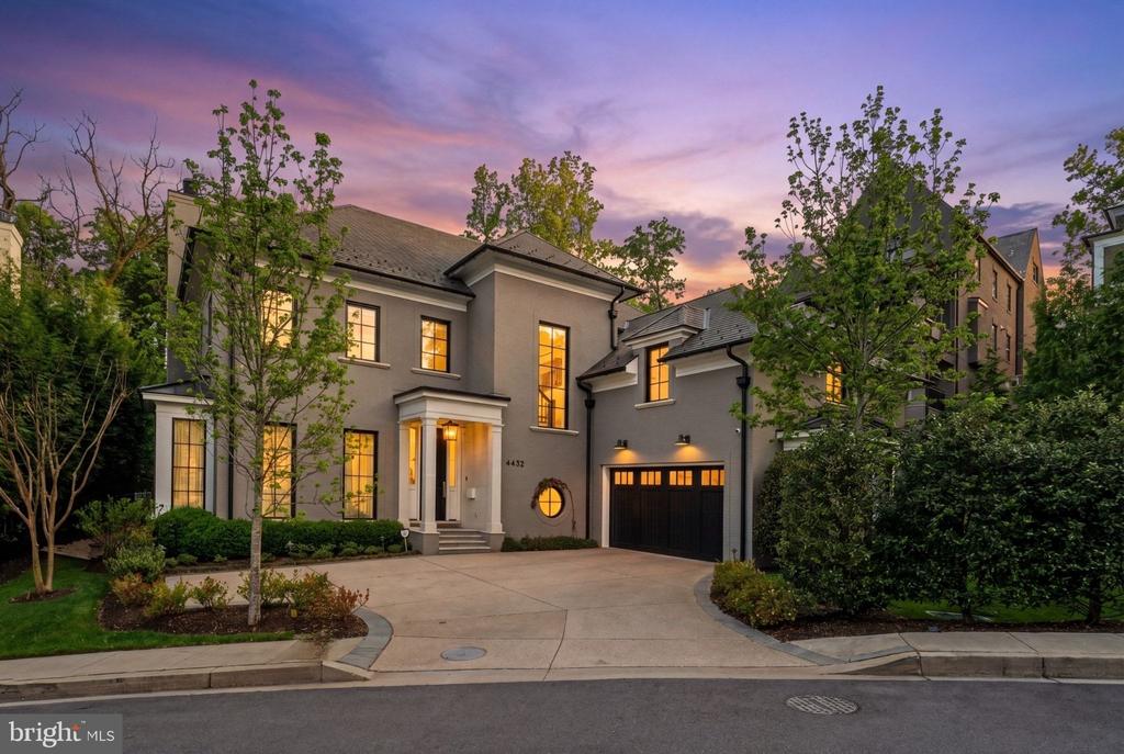 Two-story gray home at dusk with a columned entry, illuminated windows, and a black double garage.