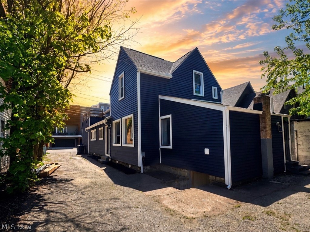 Blue-sided two-story house with a paved courtyard beneath a colorful evening sky.