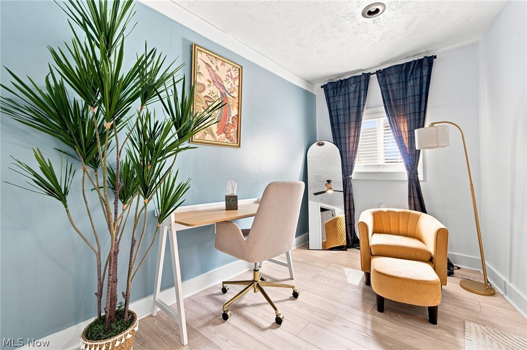 Furnished home office with a pale blue wall, mustard armchair, desk, and tall potted plant.