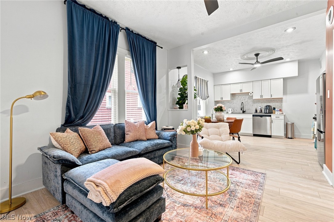 Open-plan living room with blue sectional, tall curtained windows, and white kitchen.