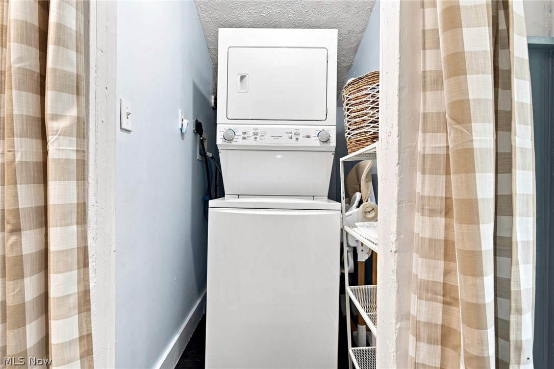 Laundry closet with a stacked white washer and dryer behind beige plaid curtains.