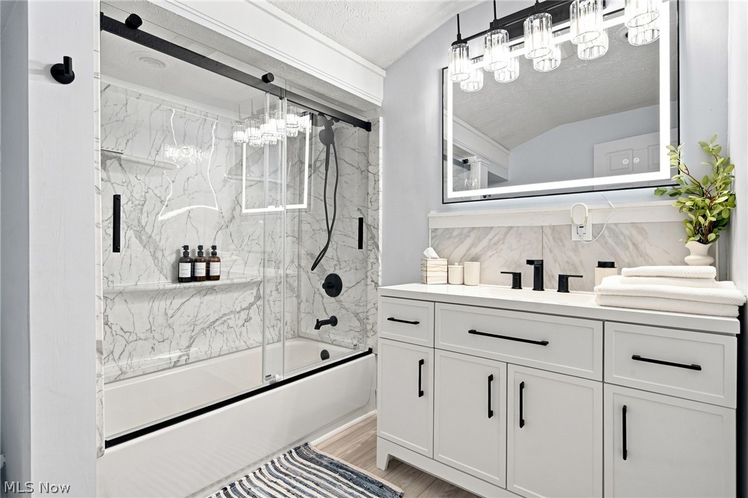 Bathroom with a glass-enclosed marble-look shower and white vanity with black fixtures.