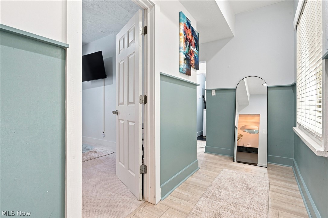 Hallway with sage-green wainscoting, pale flooring, an arched mirror, and an open doorway.