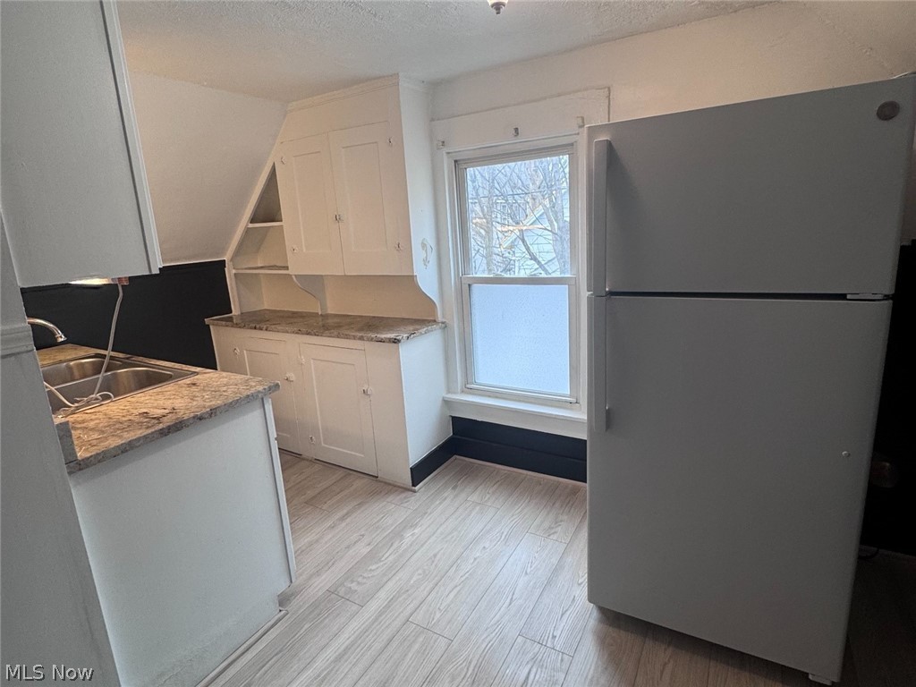 Kitchen with white cabinets, patterned countertops, light wood-look flooring, and a large refrigerator.