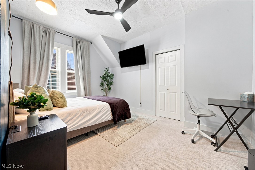 Furnished bedroom with curtained windows, a wall-mounted TV, ceiling fan, and desk.