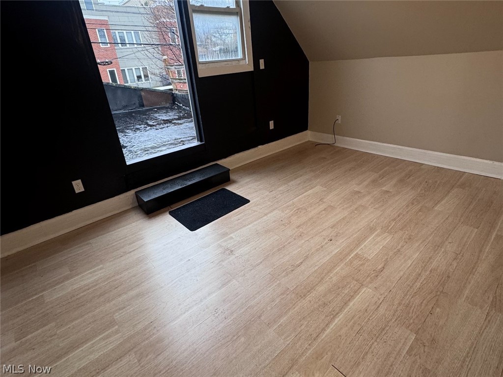 Empty room with light wood flooring, a sloped ceiling, and a glass door opening to a snowy balcony.