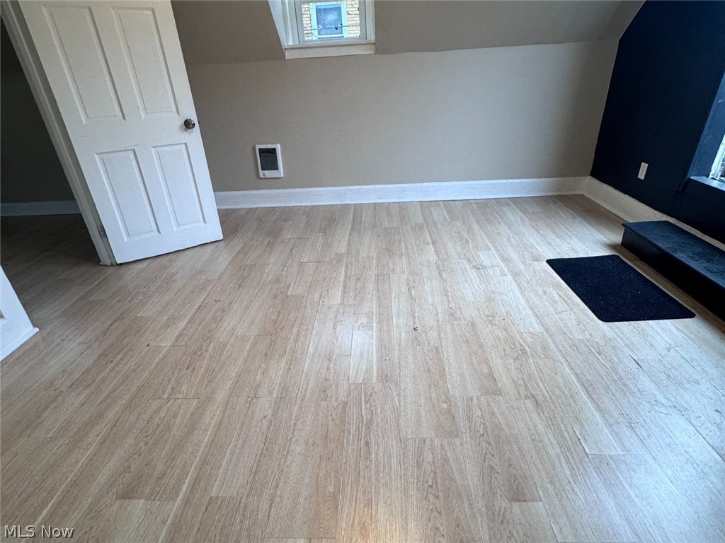 Mostly empty room with light plank flooring, a navy accent wall, and a small high window.