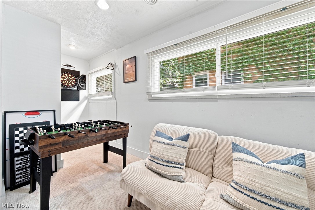 Furnished recreation room with a foosball table, dartboard, and cream sofa beneath wide windows.