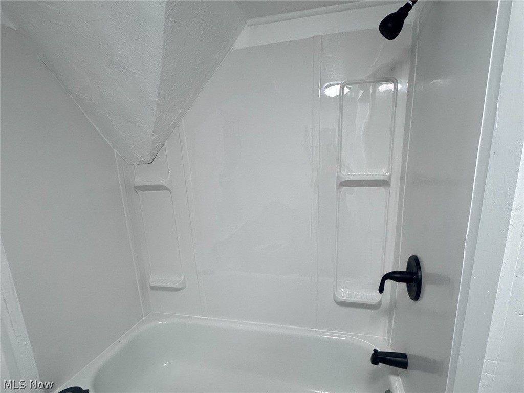 White bathtub and shower with molded shelves and black fixtures.