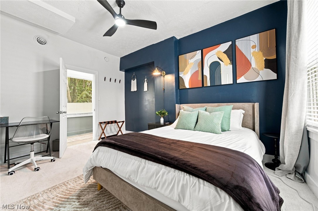 Bedroom with a navy accent wall, abstract artwork above the bed, and a desk by the door.