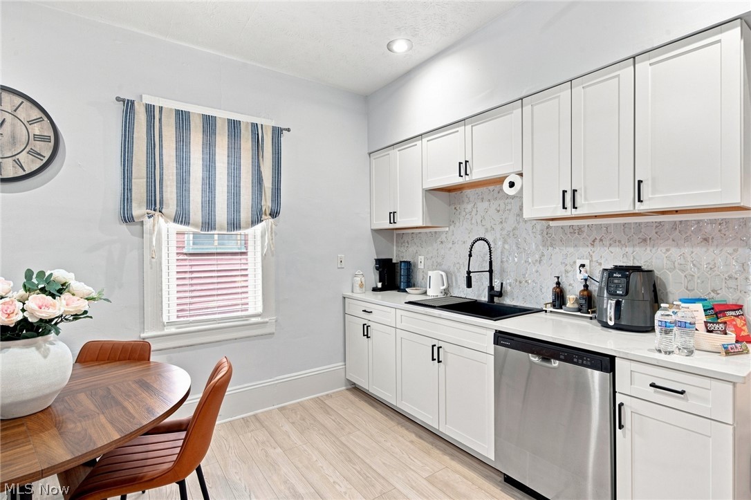 Kitchen with white cabinets, patterned tile backsplash, black countertop, and a dining table by the window.