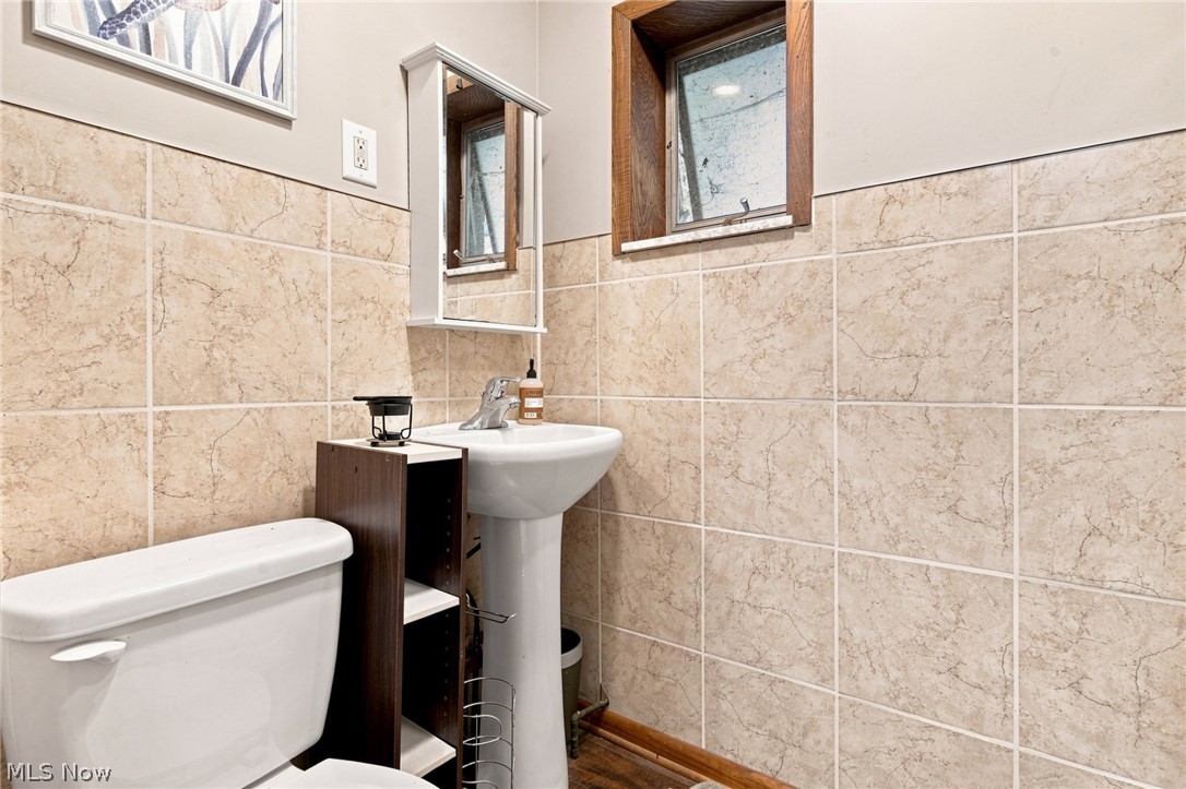 Bathroom with beige tile walls, a pedestal sink, toilet, and mirrored medicine cabinet.