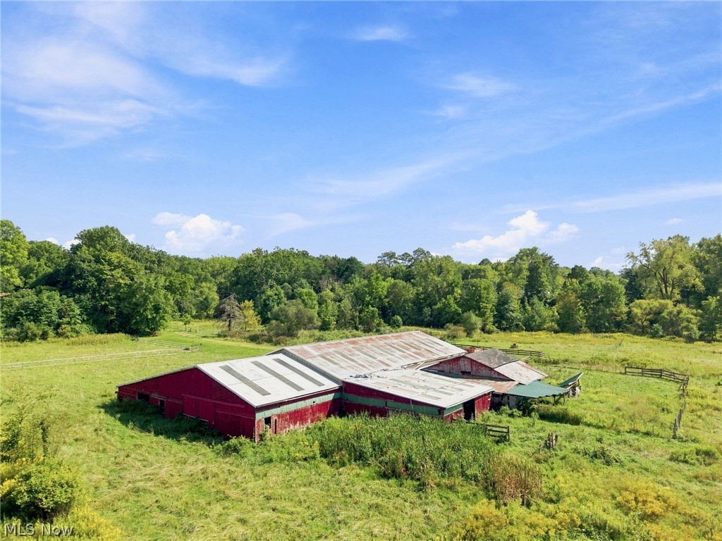 Aerial view of red farm barns amid green pasture and a wooded tree line.