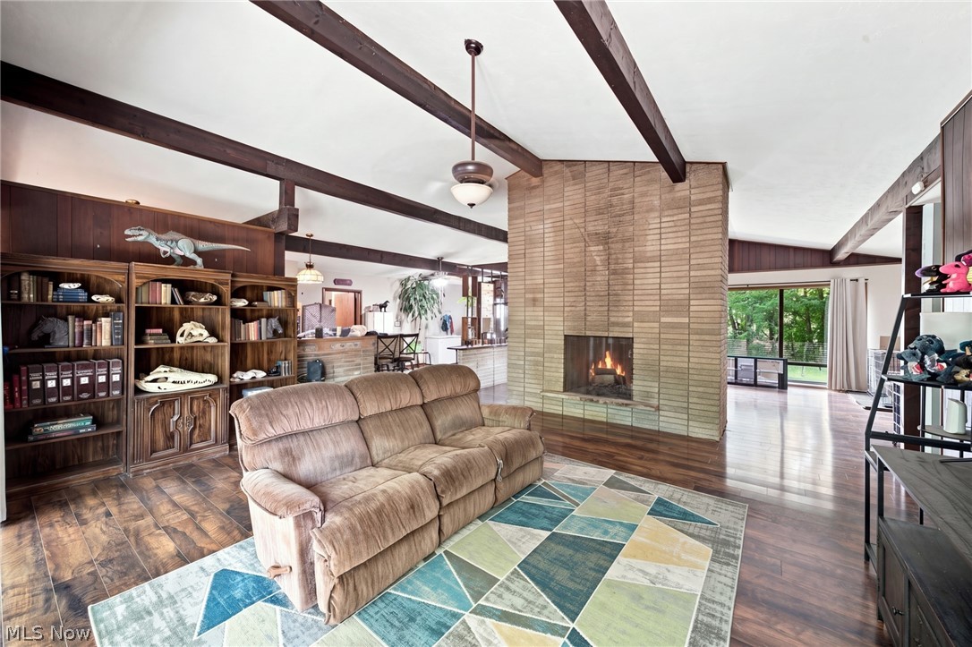 Living room with a tiled fireplace, exposed beams, fossil-filled bookcases, and a colorful geometric rug.