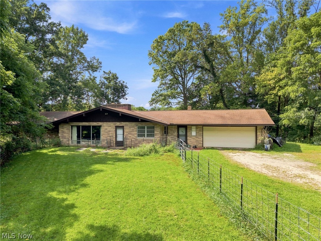 Single-story brick home with an attached garage, fenced lawn, and mature trees.