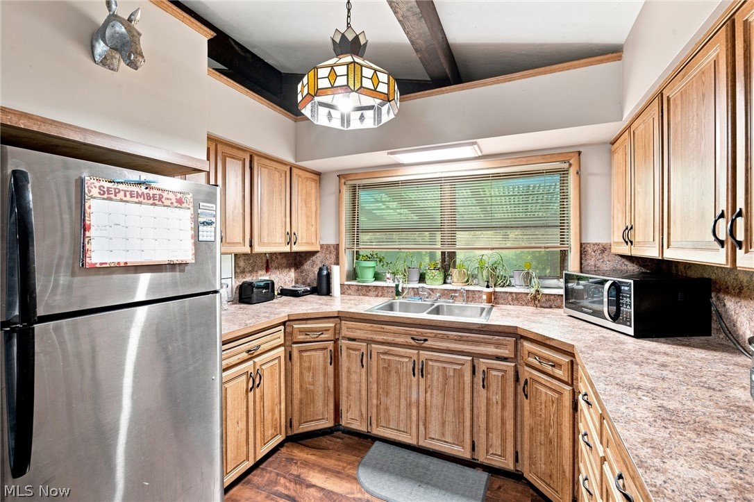 Kitchen with wood cabinets, stainless steel refrigerator, and a double sink beneath a wide window.
