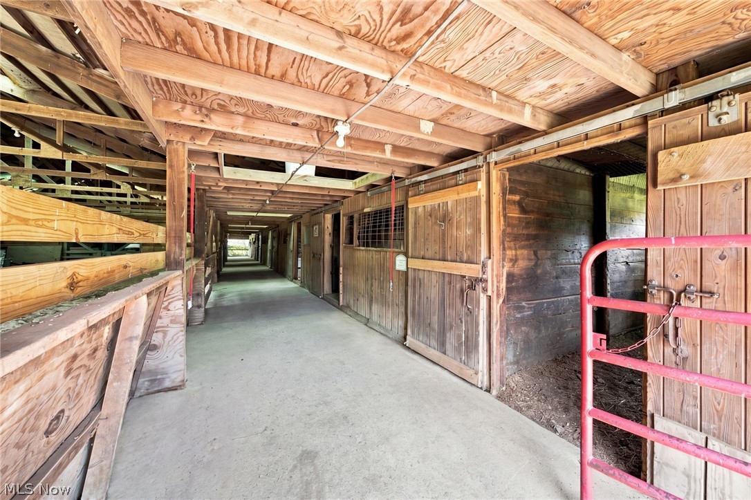 Wooden stable aisle with horse stalls on both sides and a red gate in the foreground.