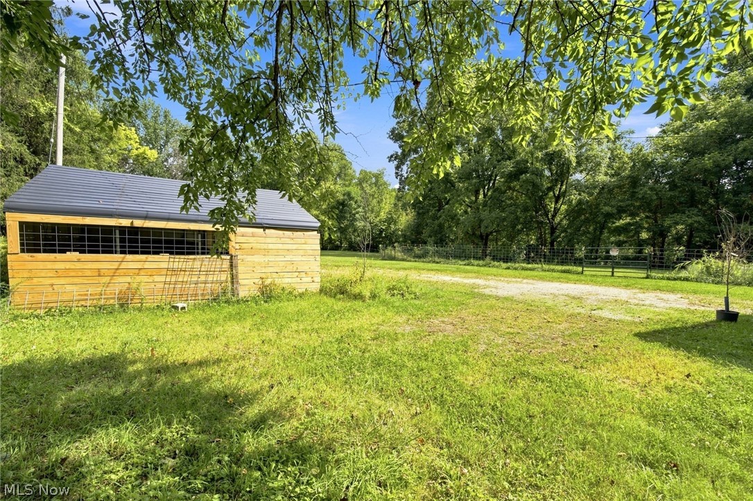 Wooden outbuilding beside a grassy yard, gravel drive, and trees.