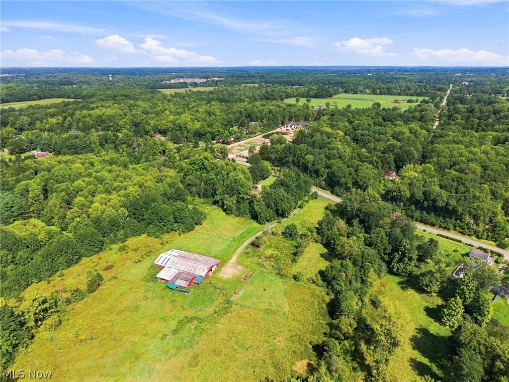 Aerial view of a rural property with open fields, a red-and-white outbuilding, and surrounding woods.