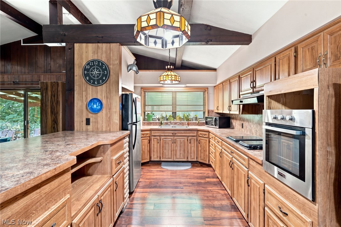 Kitchen with wood cabinets, exposed ceiling beams, stained-glass pendant lights, and a wide foreground counter.