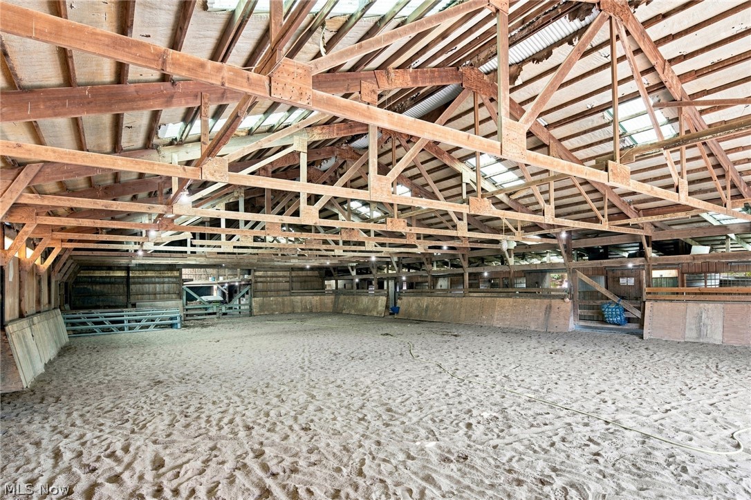 Indoor riding arena with sandy footing, exposed wooden trusses, and stalls along the sides.