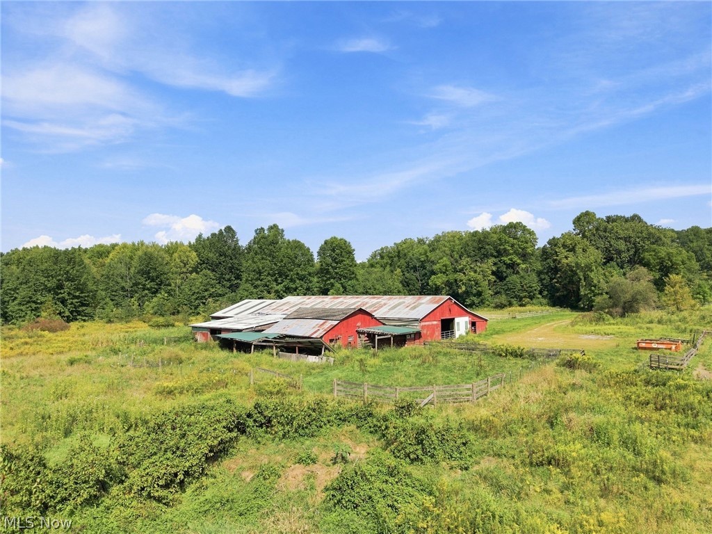 Red barn and fenced pasture amid green fields and mature trees.